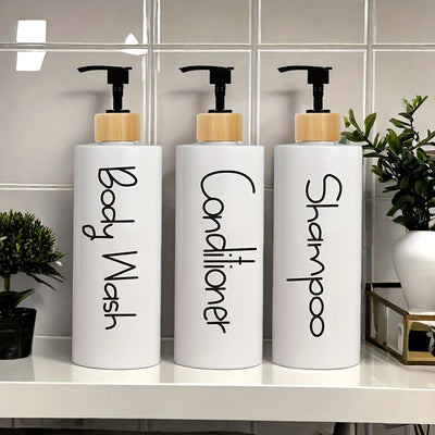 Three white bottles labeled 'Body Wash', 'Conditioner', and 'Shampoo' on a bathroom counter.